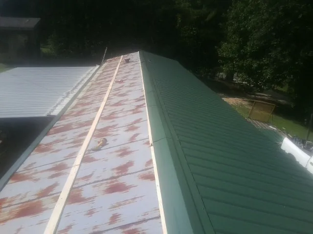 Old rusted panels beside newly installed green metal roofing — Wind Damage Roof Repair by Roofing Brothers in Hancock