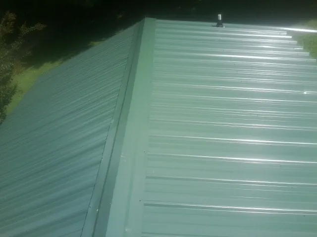 New green metal panels meeting at the ridge of a roof — Flat Roof Repair work by our crew in Hancock